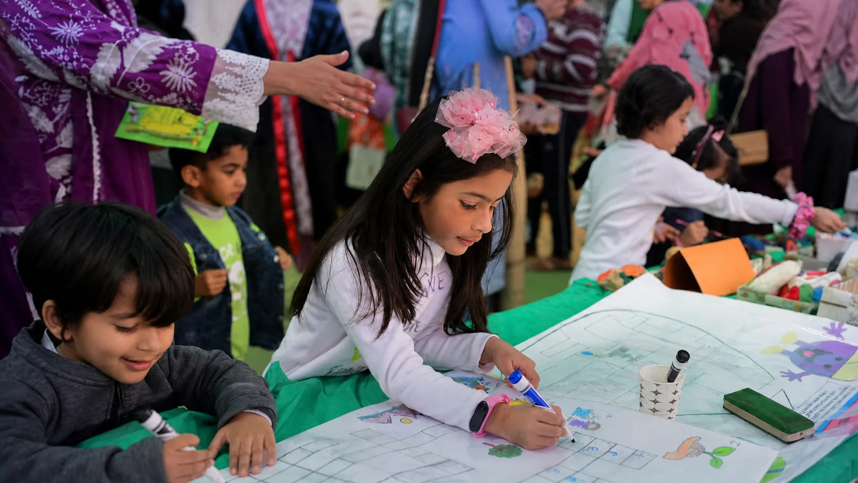 Children creating a large collaborative artwork at a lively school activity fair