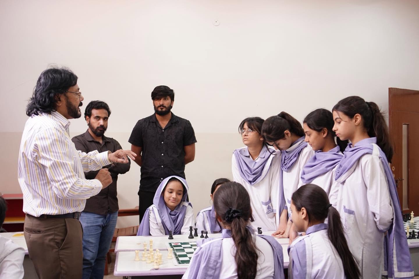 HPGS students listening to chess instruction around a board
